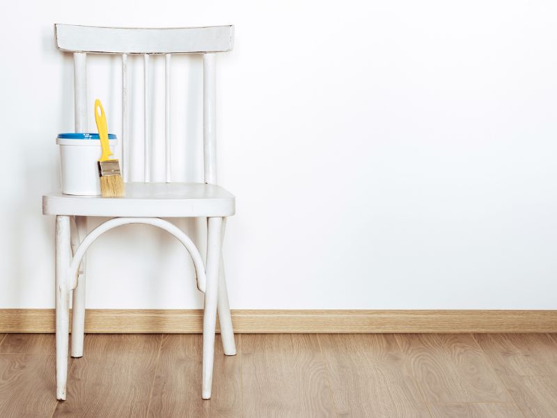 Affordable DIY projects: a white chair with a paintbrush and paint can, perfect for an upcycled furniture makeover