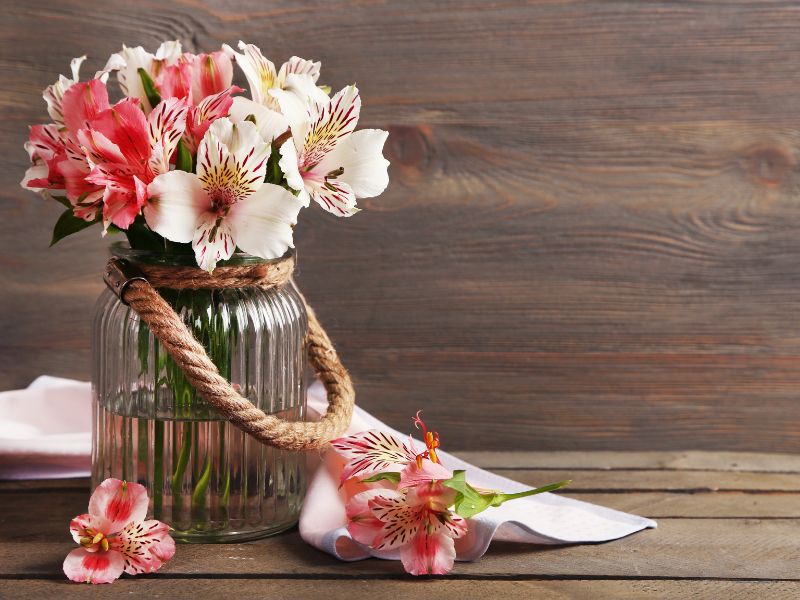 Affordable DIY projects: a rustic mason jar vase wrapped with rope, filled with pink and white flowers, perfect for home decor