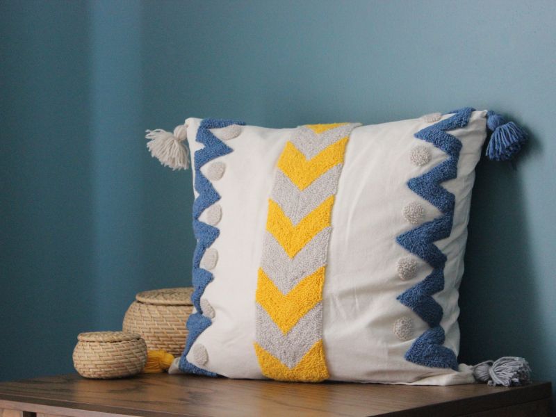 Affordable DIY projects: a handmade decorative throw pillow with colorful textured patterns and tassels, perfect for cozy decor