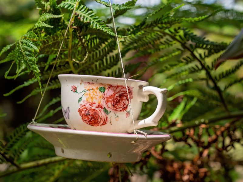 Upcycling projects: Teacup bird feeder hanging in a garden, surrounded by green foliage