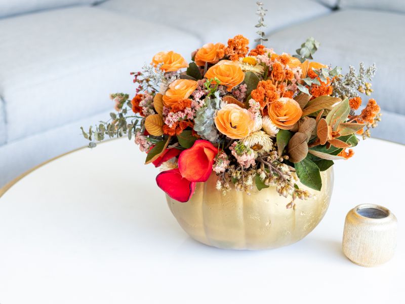 Affordable DIY projects: a vibrant floral arrangement in a gold pumpkin vase, perfect as a stylish and seasonal table centerpiece