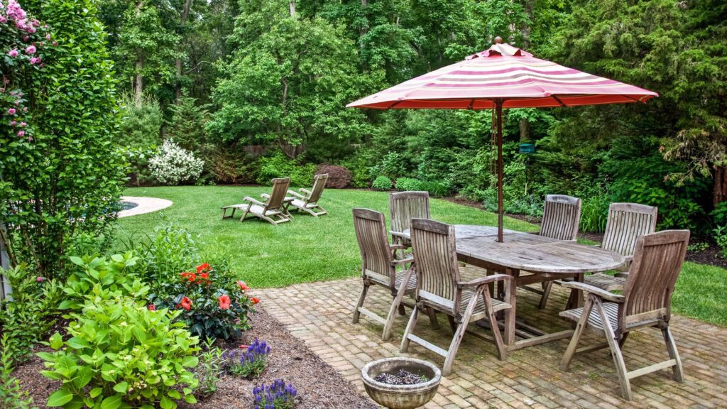  DIY outdoor decor: a cozy patio setup with wooden chairs, a large table, and a red striped umbrella surrounded by greenery